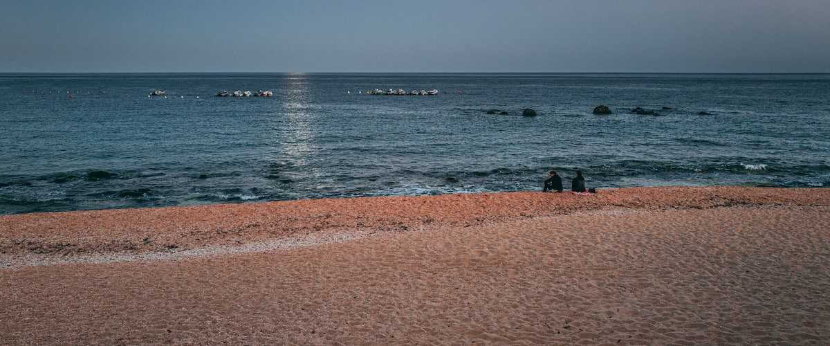 A beach with a calm sea, a visible moon, and a few scattered rocks.