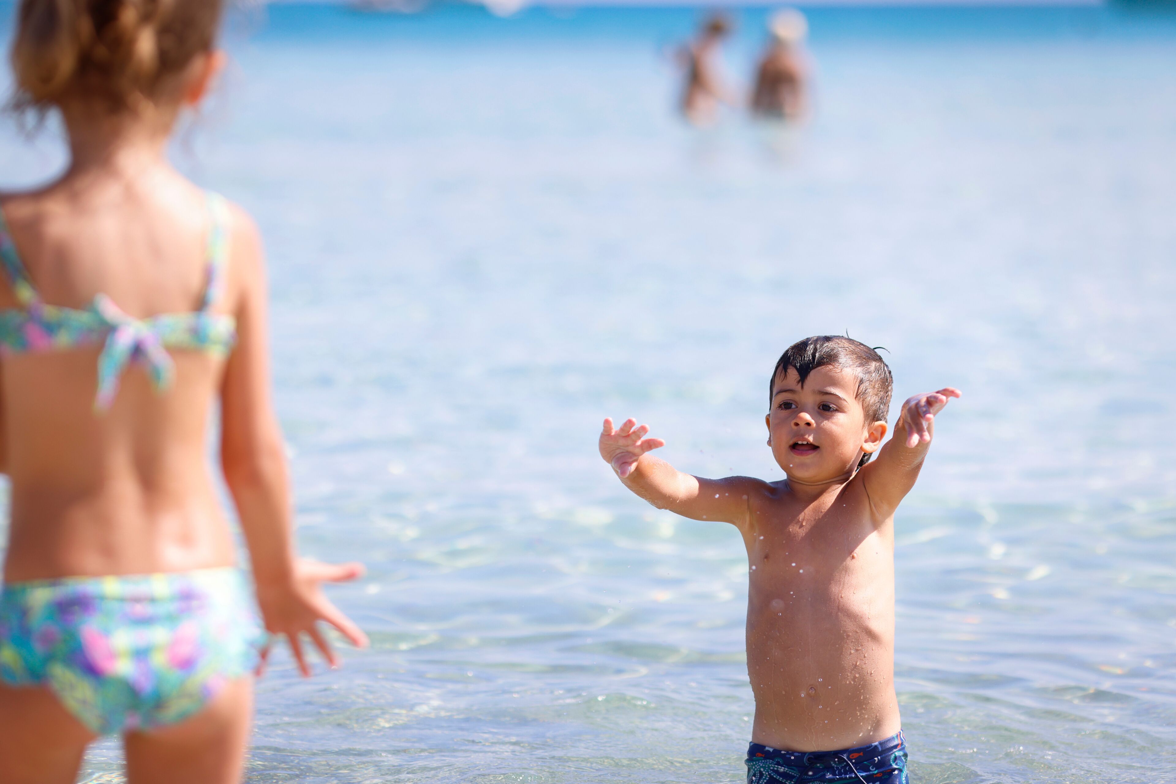 A child in the water with a clear view of the ocean and a distant shoreline.
