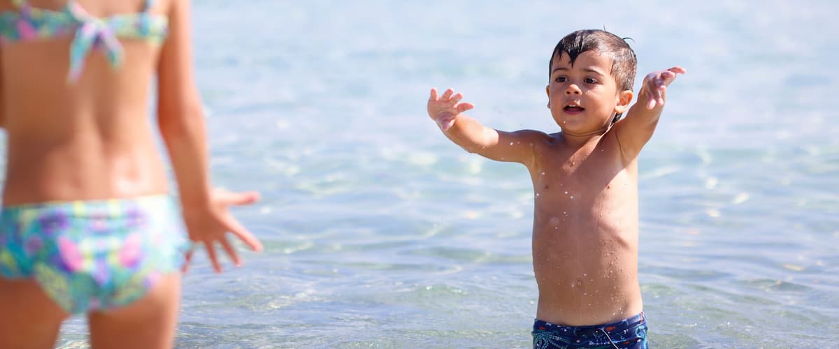 A child in the water with a clear view of the ocean and a distant shoreline.