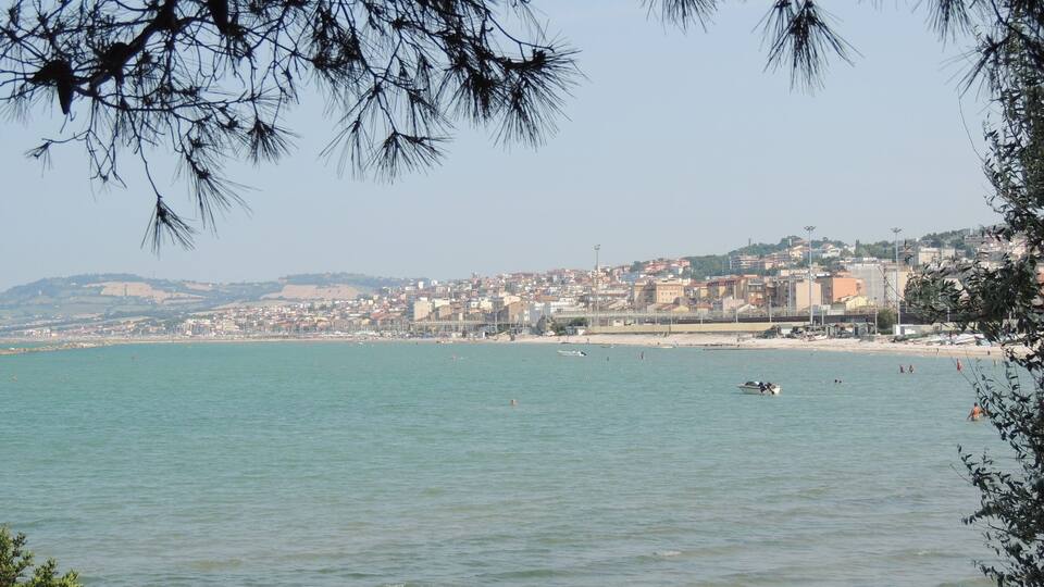 A coastal city with a beach, rocky shoreline, and a distant hill.