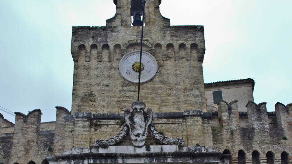 A historic stone gate with a clock tower, featuring arched windows and a weather vane.