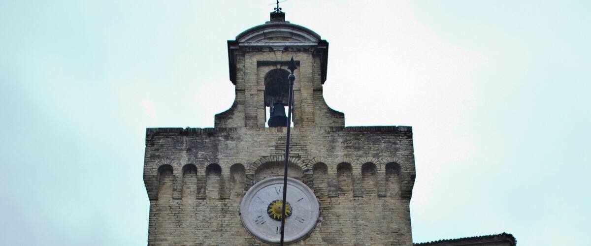 A historic stone gate with a clock tower, featuring arched windows and a weather vane.