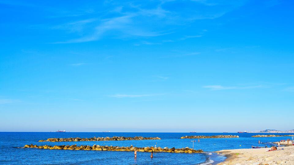 A beach with rocky breakwaters, calm blue waters, and a clear sky.