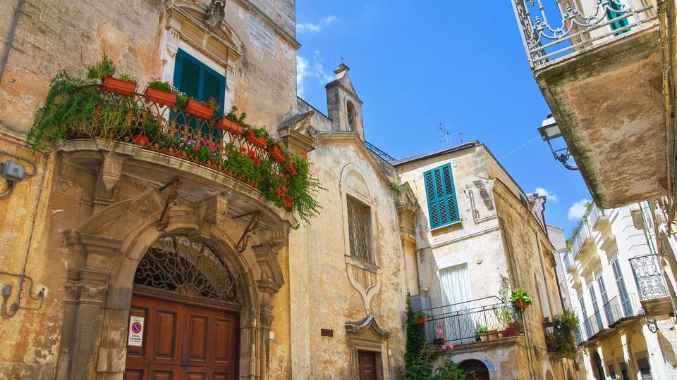 A narrow street with old buildings, a wooden door, and a balcony with plants.