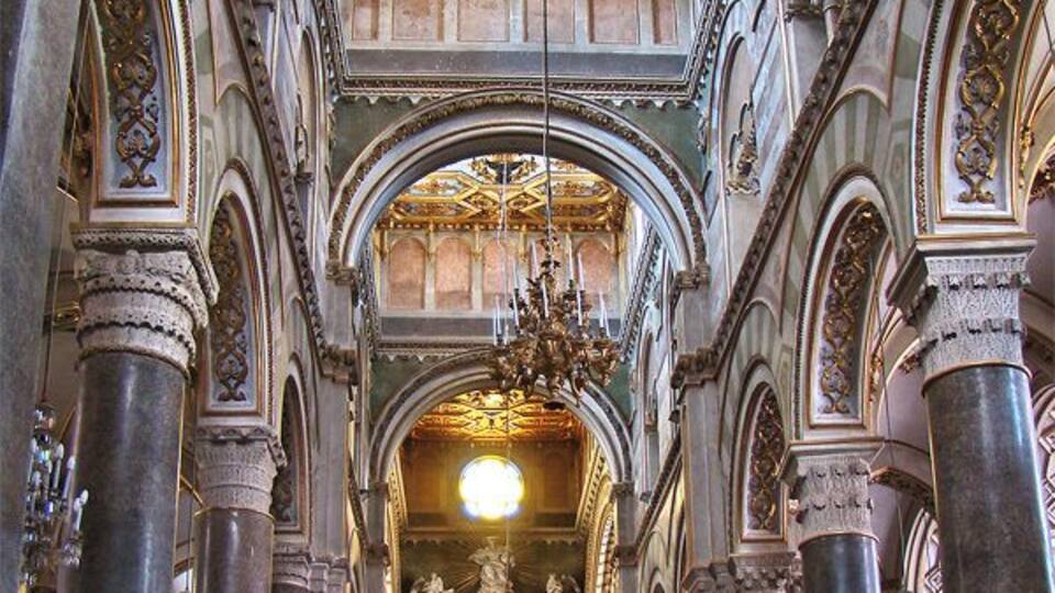 An ornate church interior with high ceilings, detailed gold decorations, and large columns.