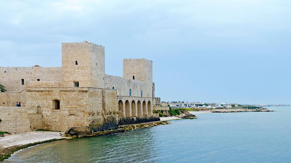 A historic stone fortress by the sea with arched windows and towers.