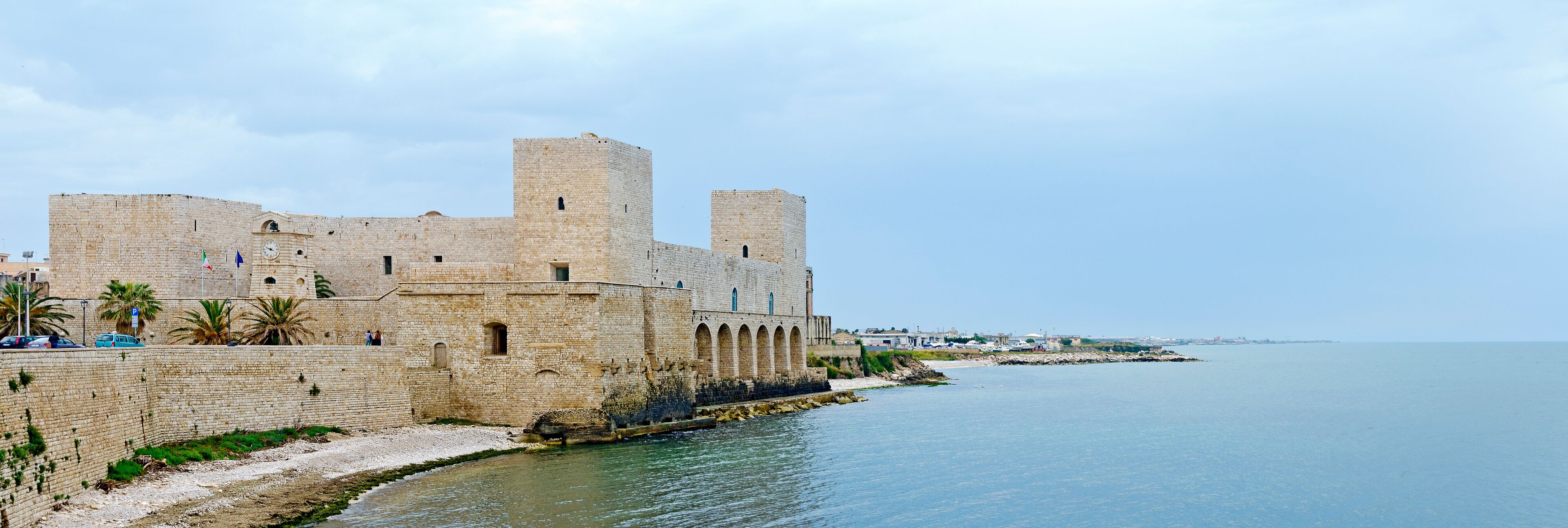 A historic stone fortress by the sea with arched windows and towers.