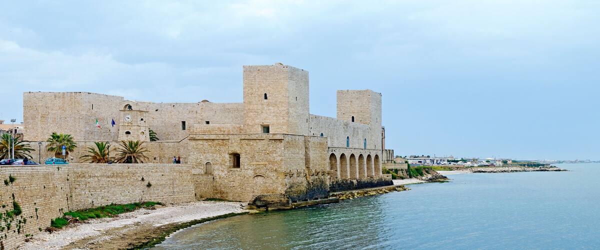 A historic stone fortress by the sea with arched windows and towers.