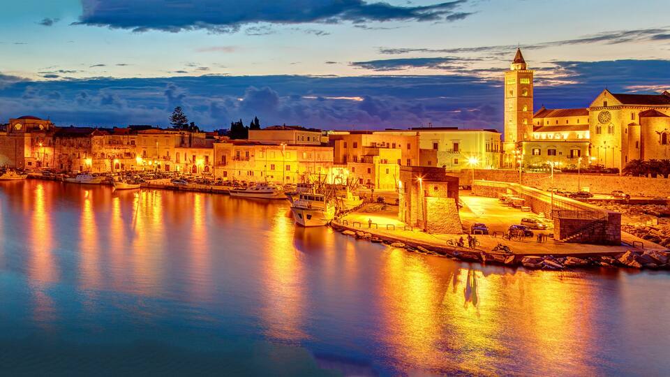 A coastal town at dusk with illuminated buildings and a prominent tower by the waterfront.