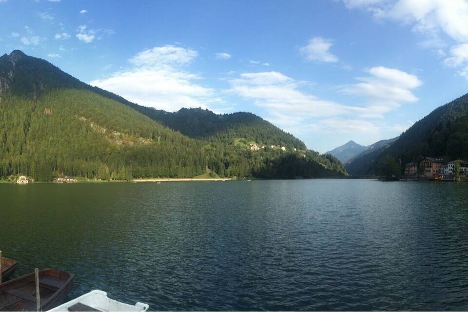A lake surrounded by mountains, a dock with boats, and buildings along the shore.