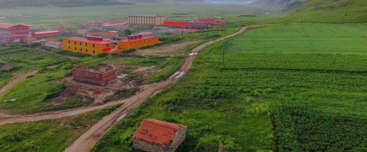 A rural landscape with green fields, a dirt road, and several buildings with red roofs.