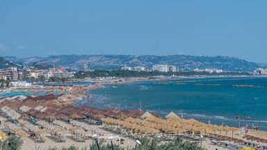 A coastal city with a beach, umbrellas, and buildings.