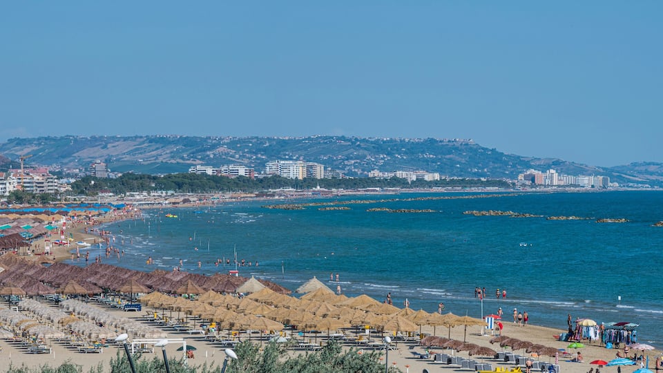 A coastal city with a beach, umbrellas, and buildings.