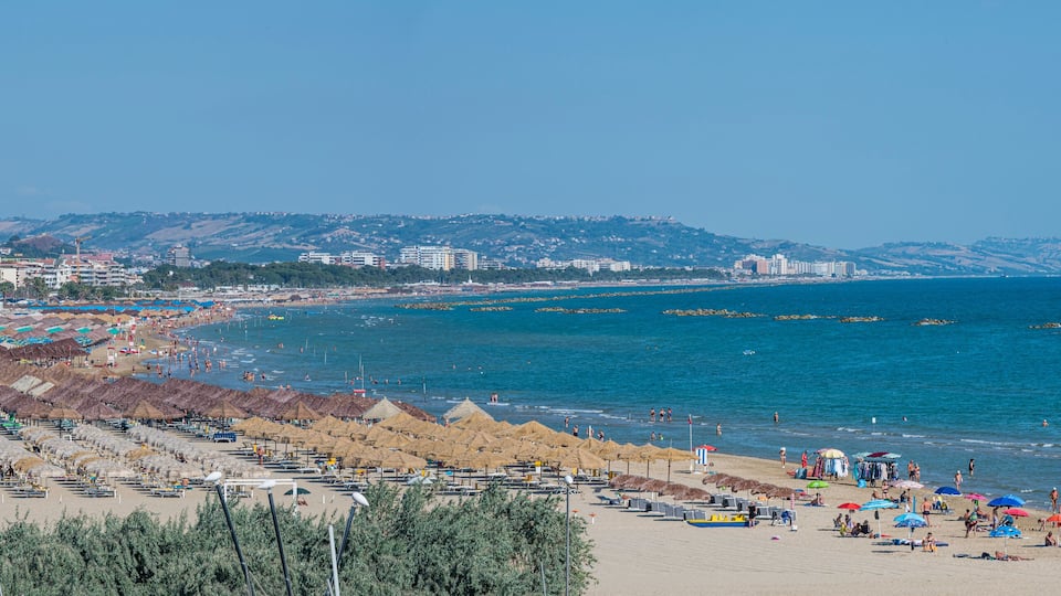 A coastal cityscape with a beach, umbrellas, and a clear blue sea.