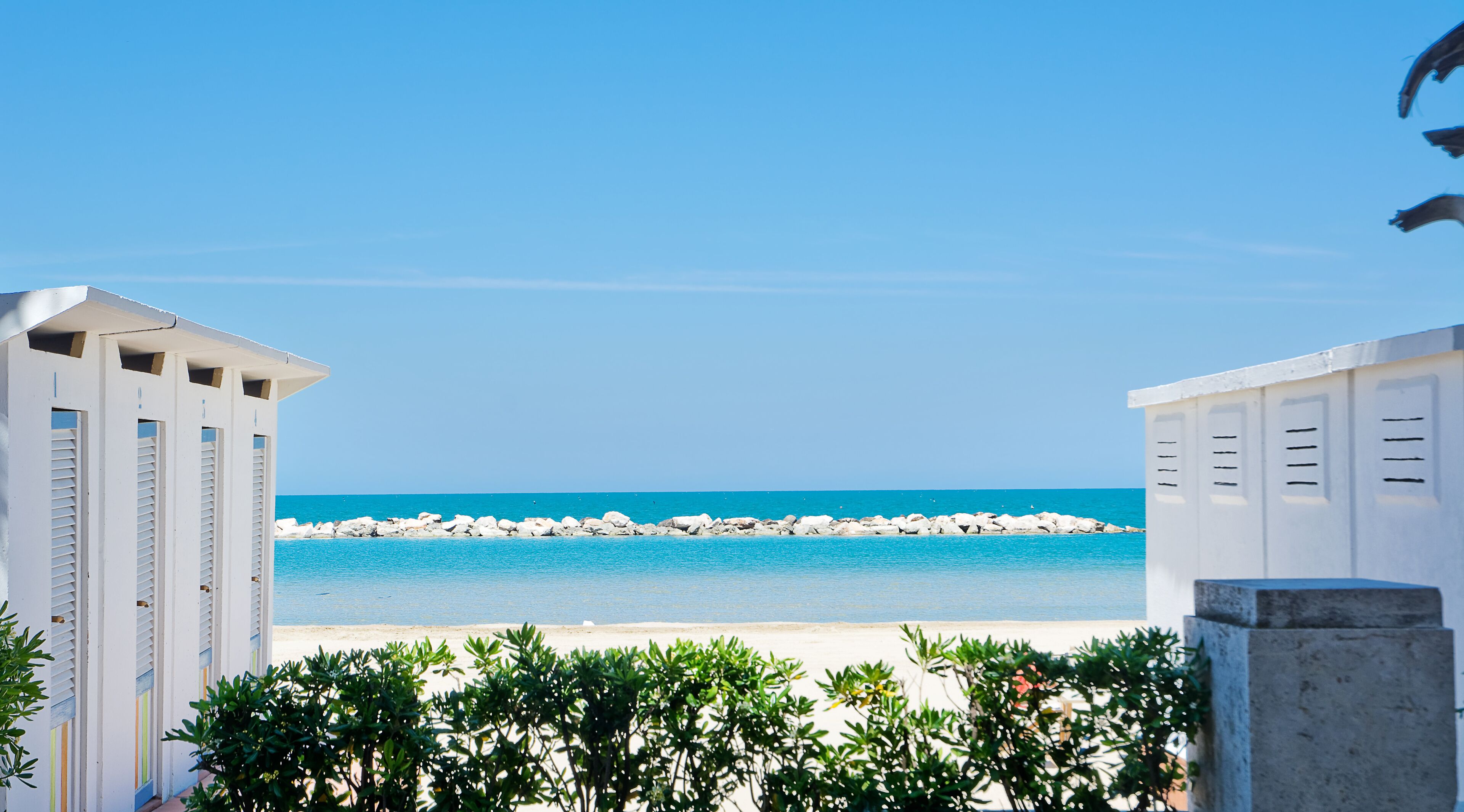Una spiaggia con acque cristalline blu, edifici bianchi e un litorale roccioso.