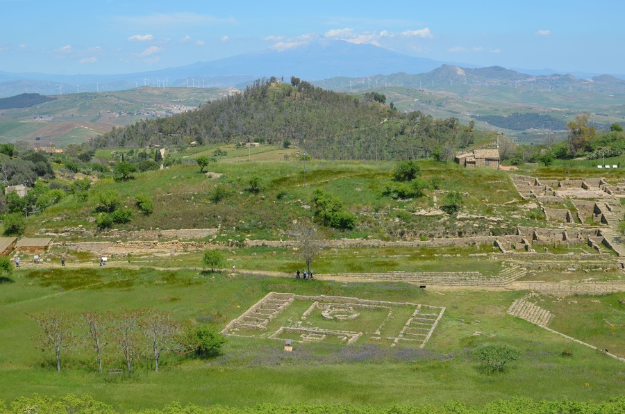 A view of Morgantina's Hellenistic agora. In the foreground the Macellum dating from the Roman period can be seen. In the background the Cittadella hilltop is visible, which was the location of Morgantina's Iron Age settlement. Mount Etna is seen in the far distance.