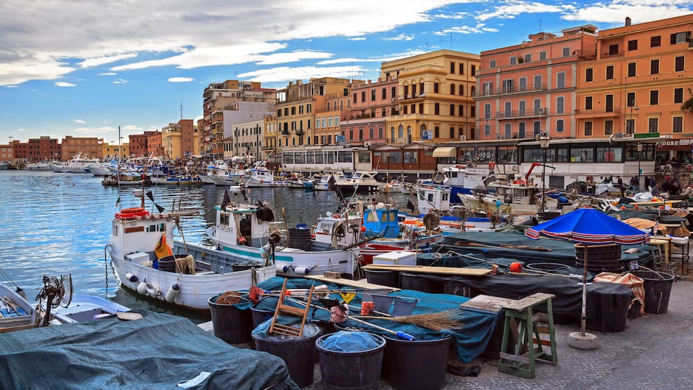 A harbor with boats docked, a blue umbrella, and buildings along the waterfront.