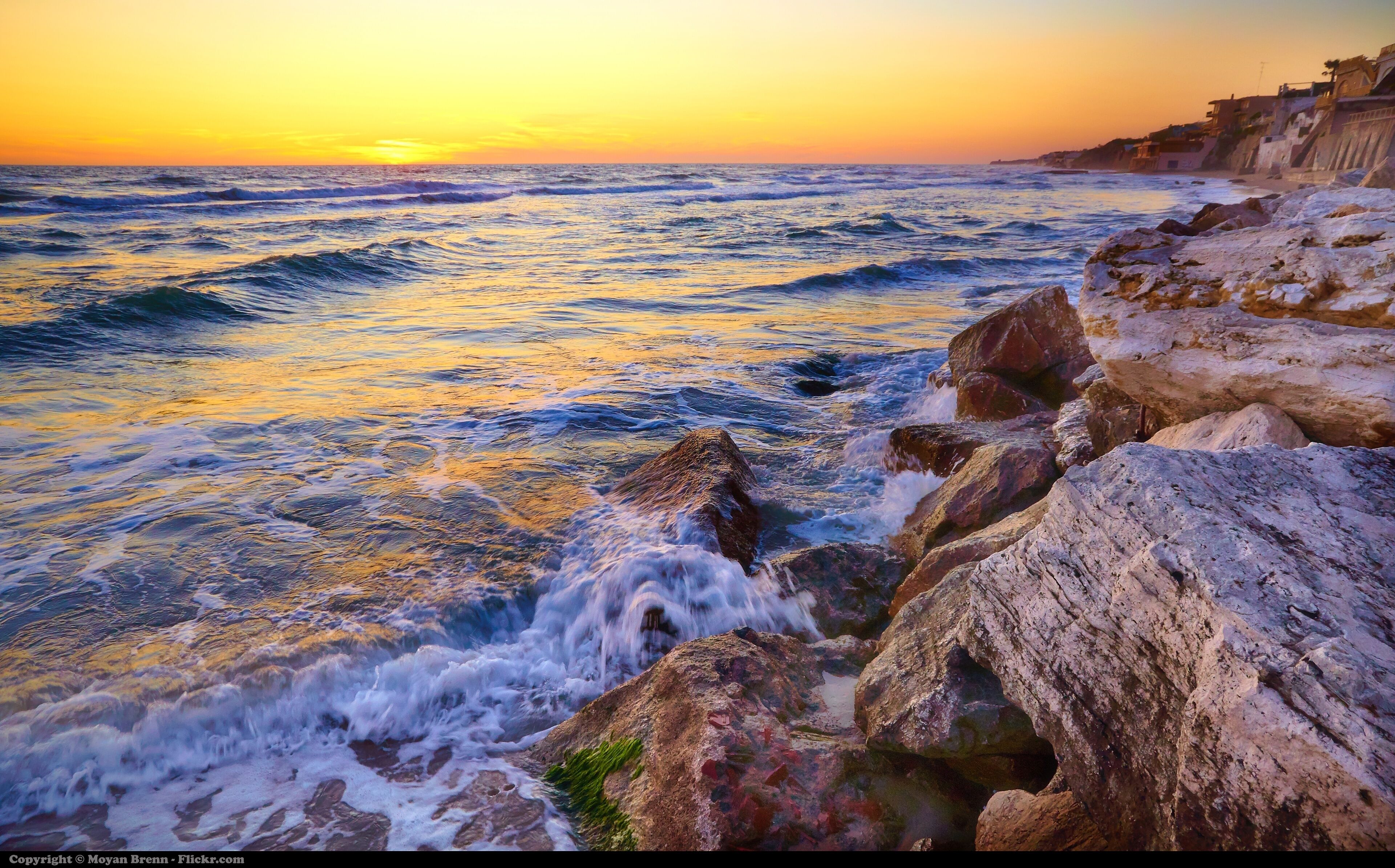 A rocky coastline with waves crashing against the rocks during sunset.
