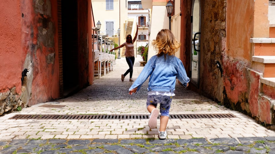 A cobblestone street flanked by buildings with red and white facades, a narrow alleyway, and a person walking away from the camera.
