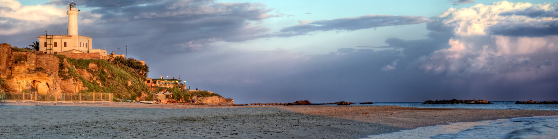 Uma praia com um farol e falésias rochosas.