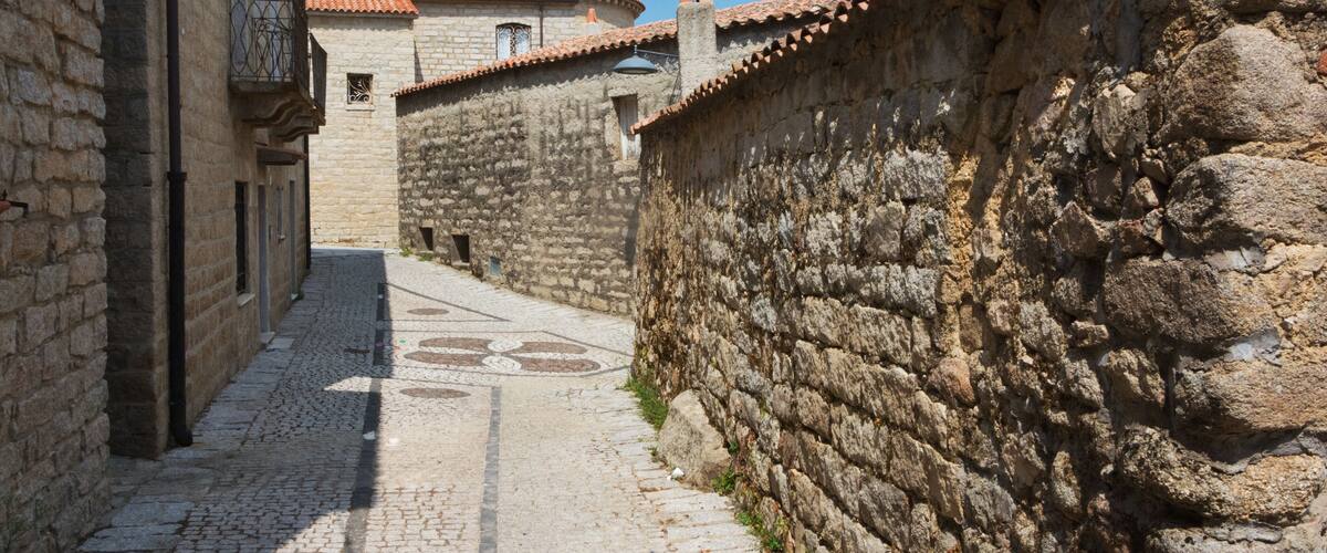 A narrow cobblestone street flanked by stone buildings with tiled roofs and a stone wall.