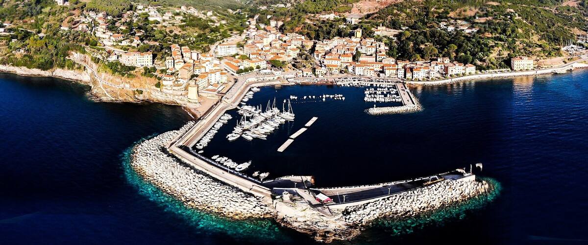 An aerial view of a coastal town with a marina surrounded by hills.