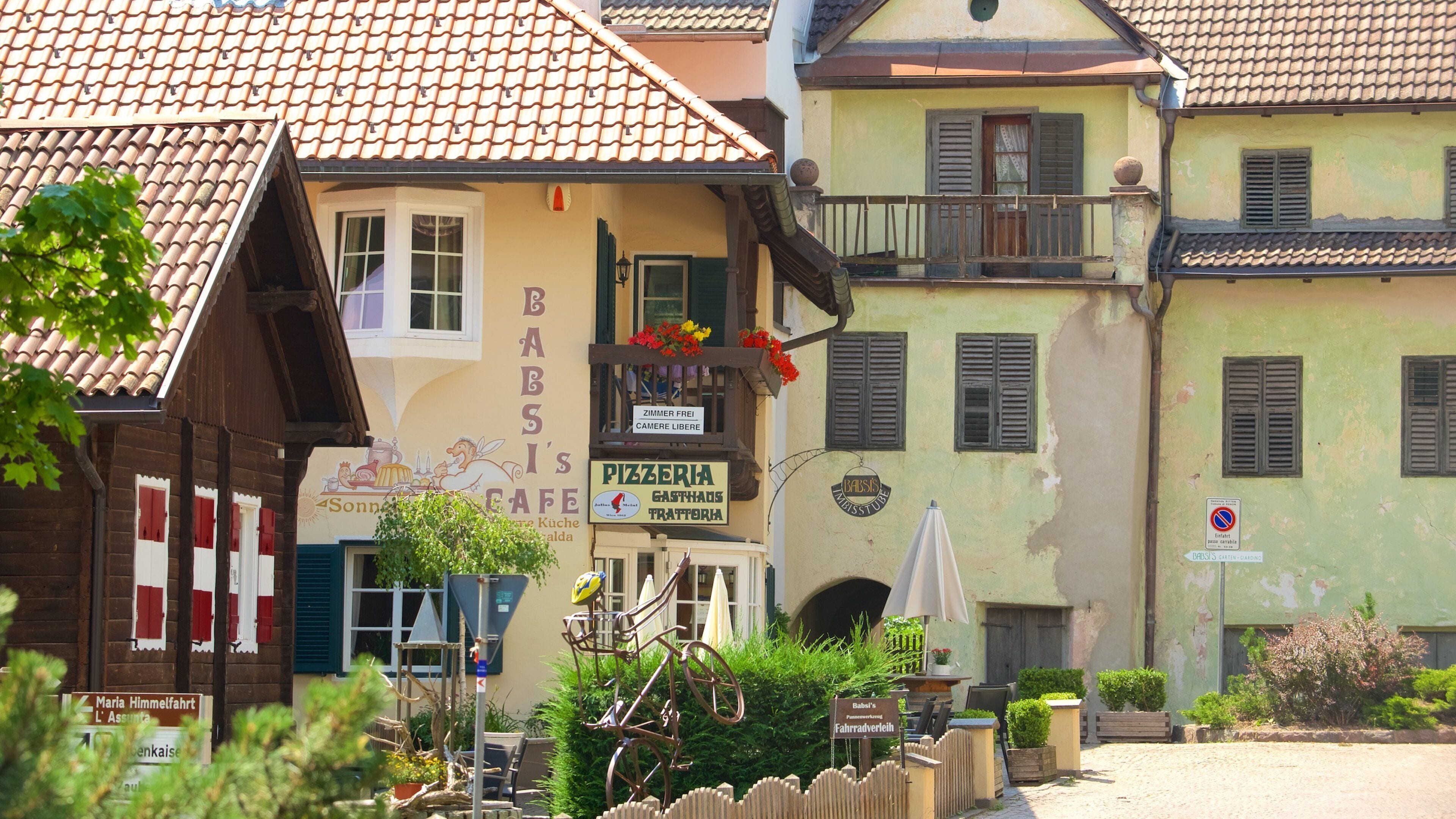 A charming European street with a pizzeria, a cafe, and a bicycle parked in front.