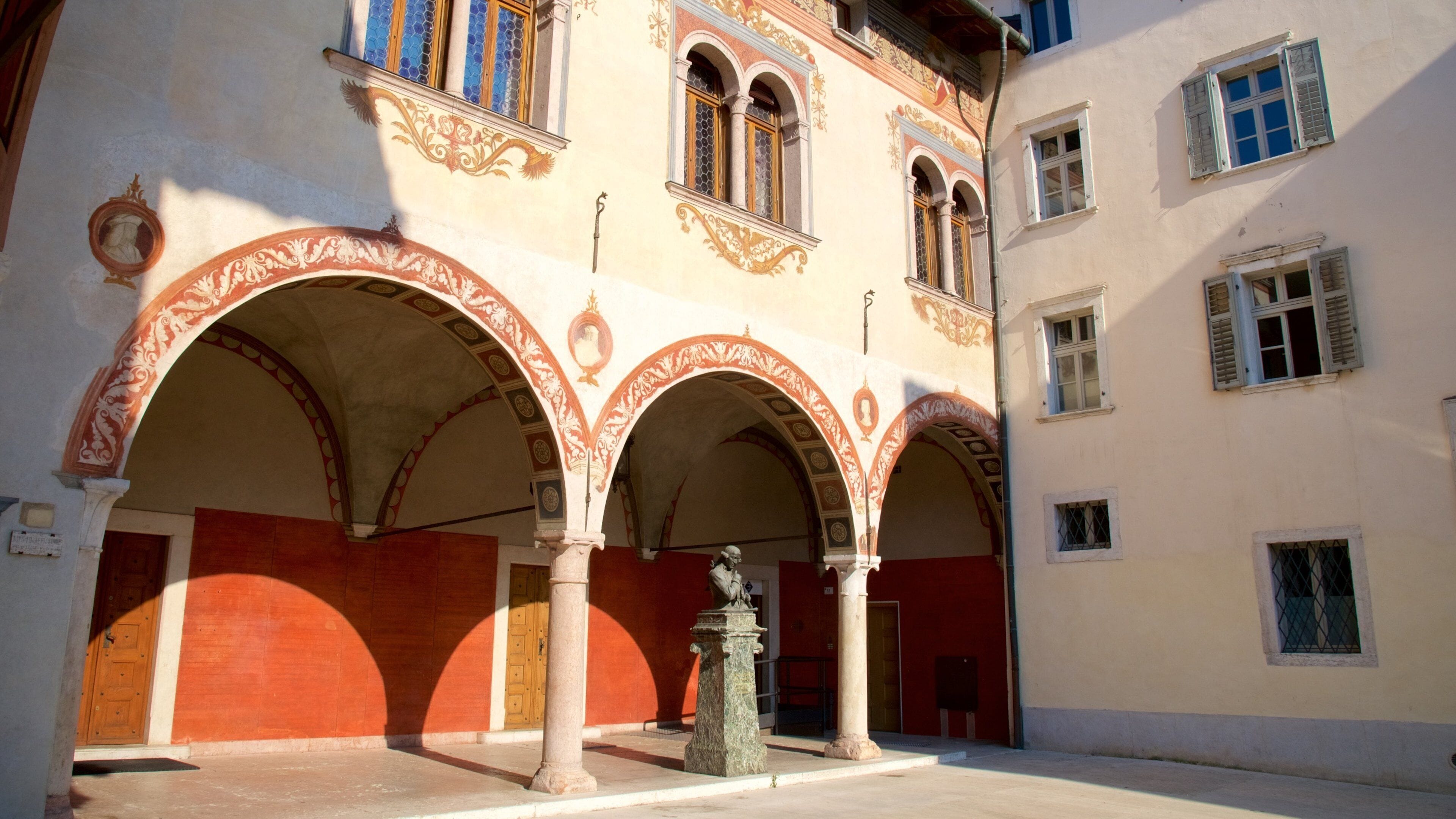 A courtyard with arches, a statue, and a building with decorative windows.