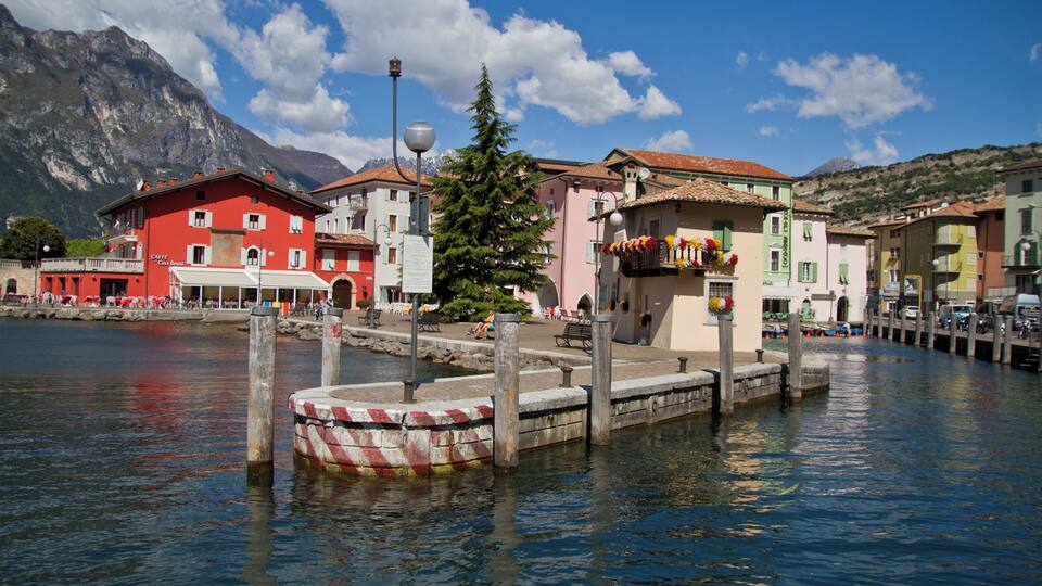 A waterfront with colorful buildings, a pier, and mountains in the background.