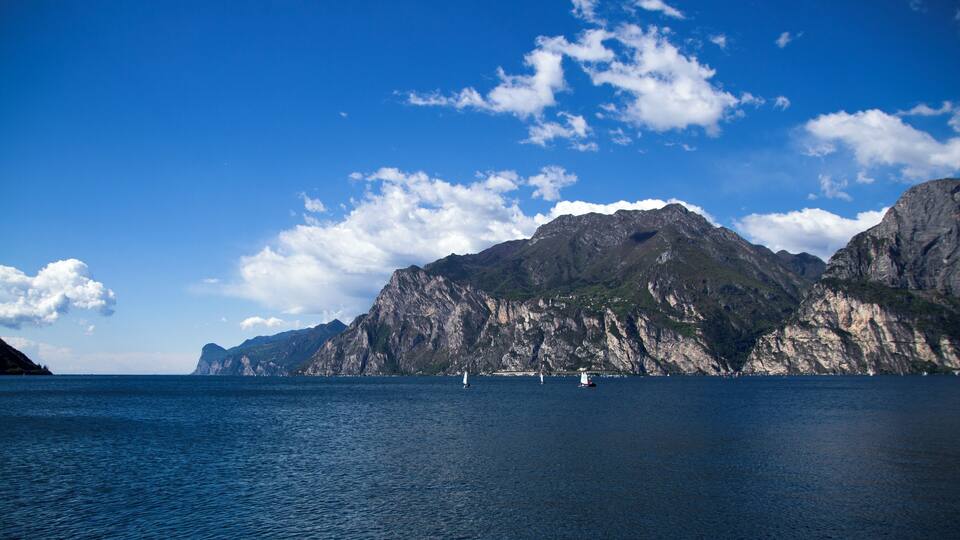 A mountainous coastline with clear blue waters and a few sailboats.