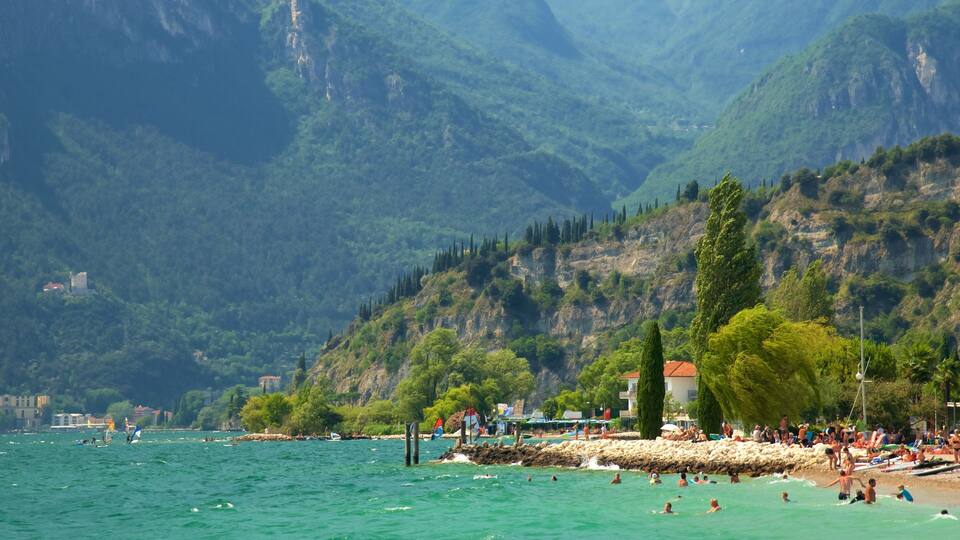 A coastal area with a rocky shoreline, people swimming and sunbathing, and a backdrop of green mountains.