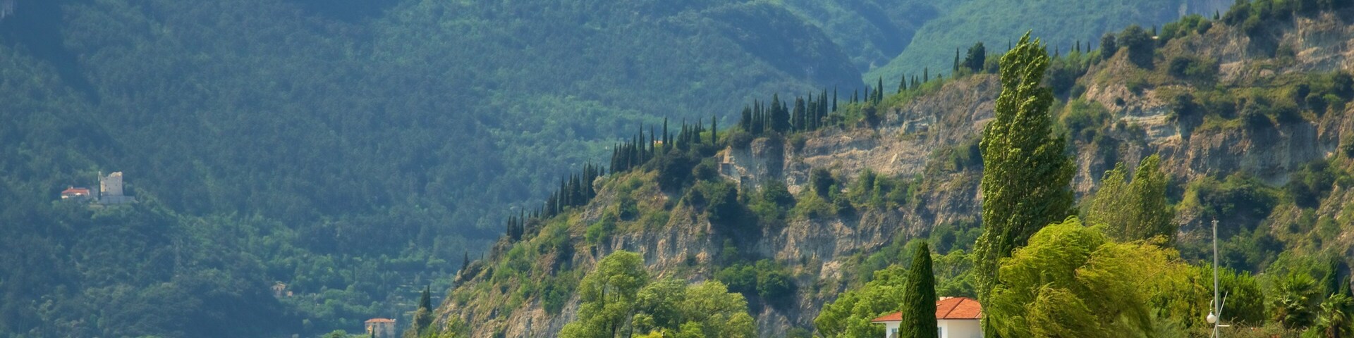 A coastal area with a rocky shoreline, people swimming and sunbathing, and a backdrop of green mountains.