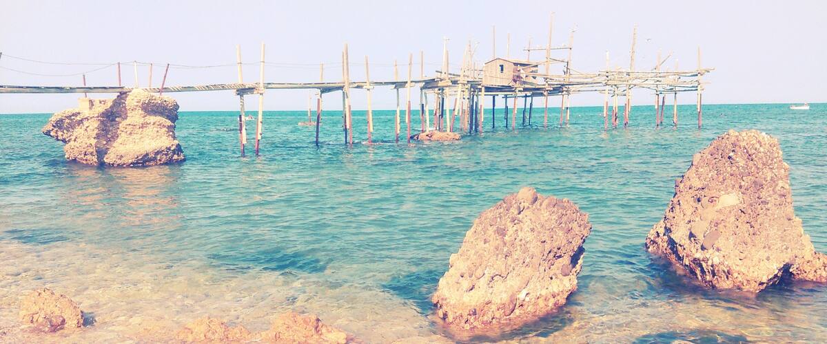 A coastal scene with clear turquoise water, rocky formations, and a wooden pier structure.