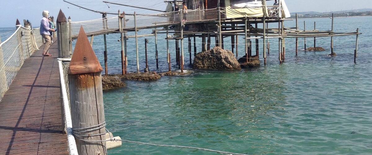 A wooden pier extending into clear blue water with a small structure on it.