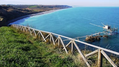 A coastal landscape with a wooden fence overlooking a beach and a small structure in the water.