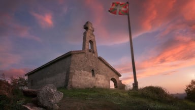 A stone church with a flagpole and a flag, set against a sunset sky.