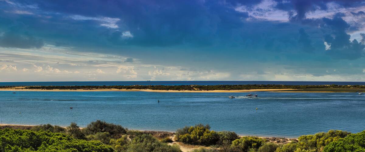 A coastal landscape with a clear sky, calm sea, and boats.