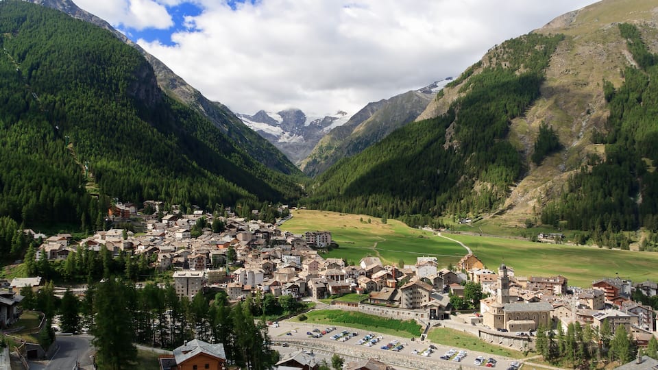 A mountainous town with a central church, surrounded by lush forests and a valley.