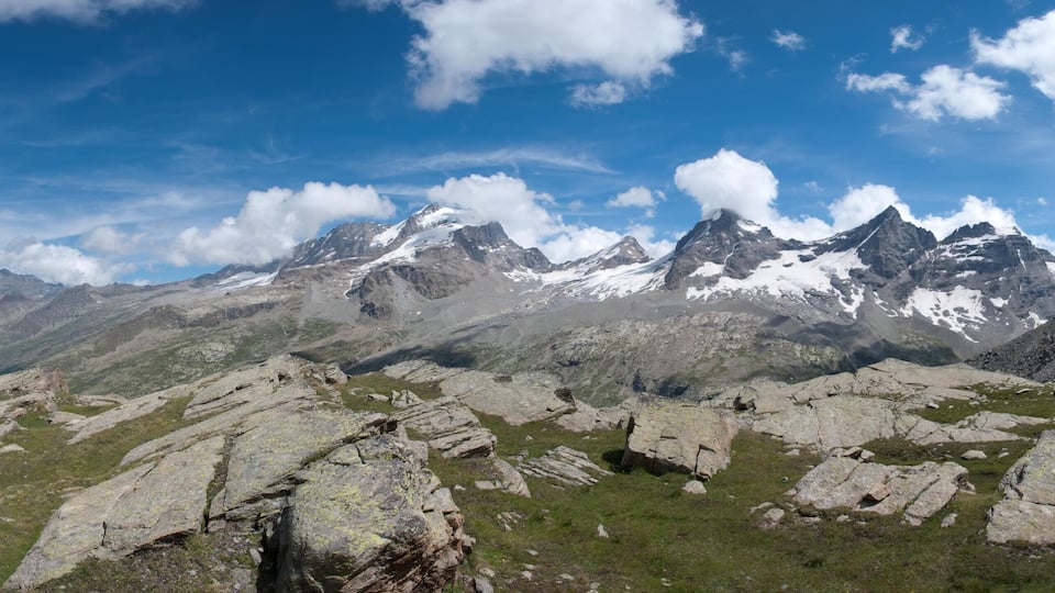 A mountainous landscape with rocky terrain and patches of grass under a clear blue sky.