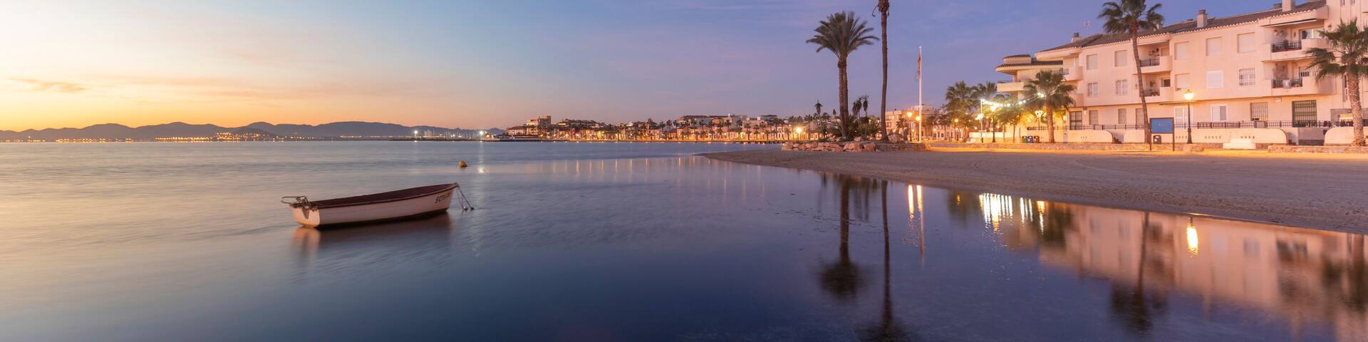 View of the Espejo beach in Los Alcazares, Region of Murcia, Spain, at sunrise and with a boat and palm trees in the background