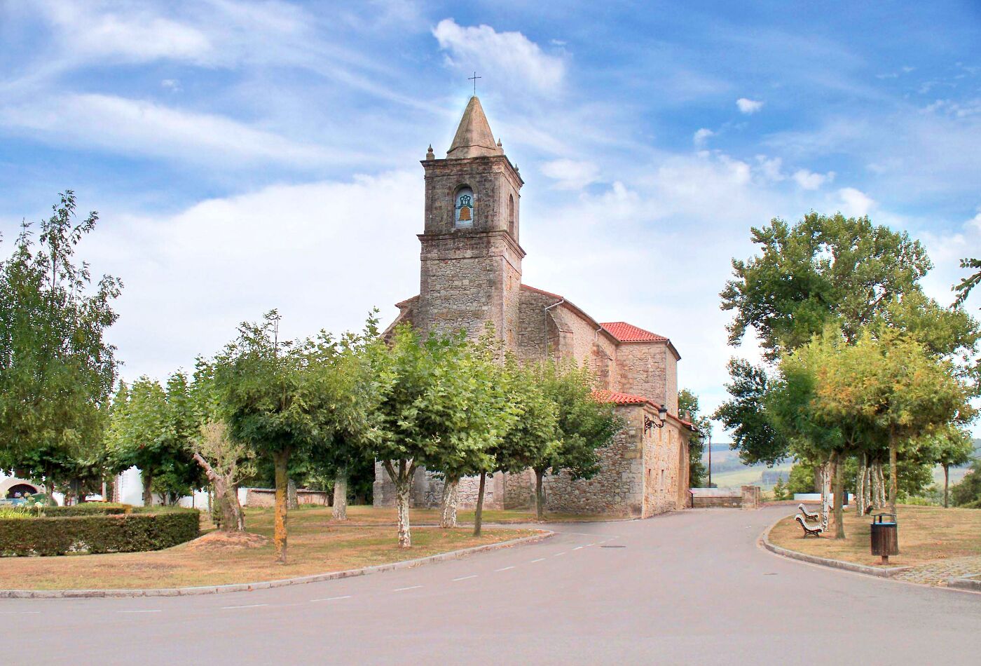 A church with a bell tower, surrounded by trees and a clear sky.