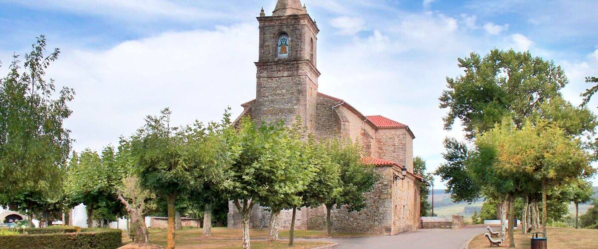 A church with a bell tower, surrounded by trees and a clear sky.