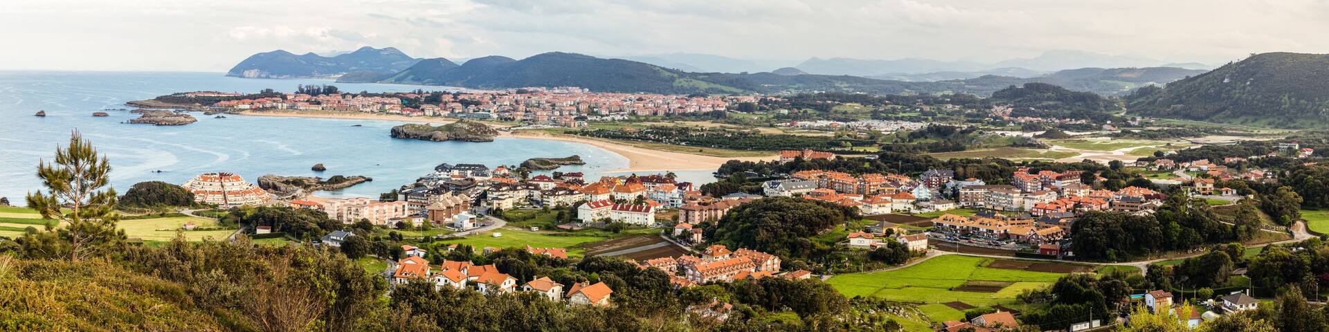 A coastal town with a beach, houses, and mountains in the background.