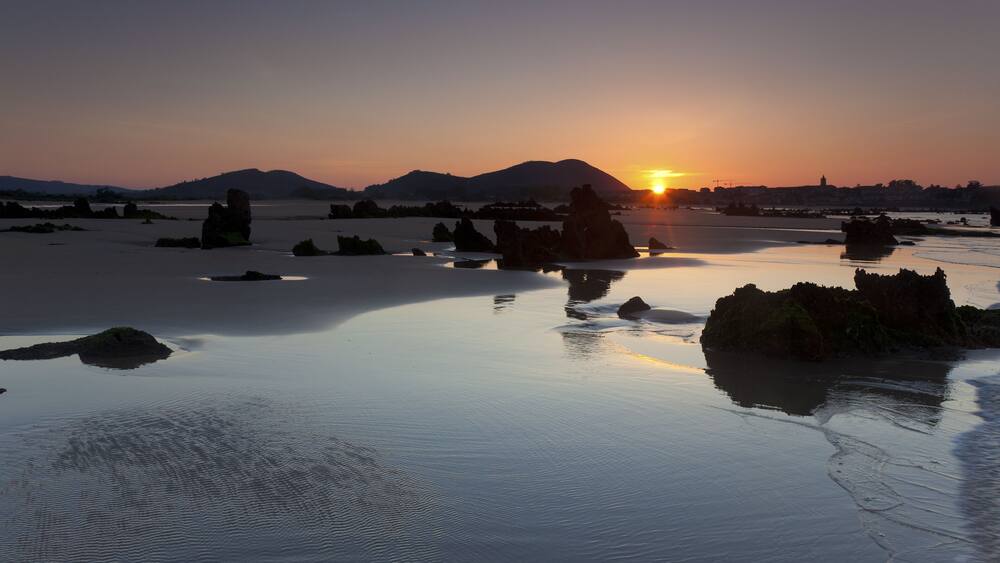 Ein Sonnenuntergang über einem ruhigen See mit verstreuten Felsen und fernen Bergen.