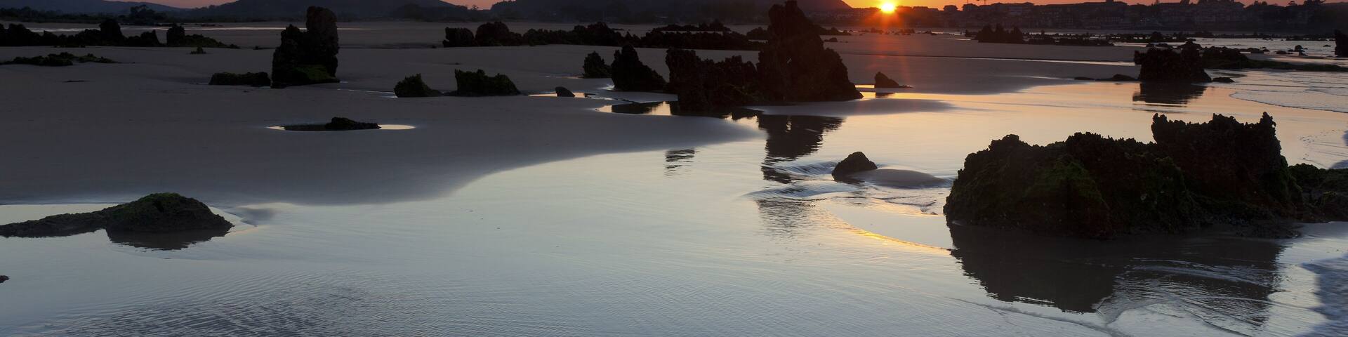 A sunset over a calm lake with scattered rocks and distant mountains.