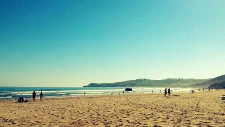 A wide sandy beach with footprints and people walking.