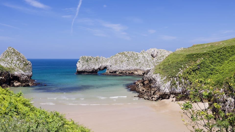 A coastal landscape with a sandy beach, rocky formations, and clear blue waters.