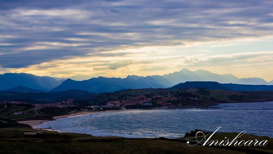 A coastal landscape with mountains in the background and a town along the shoreline.