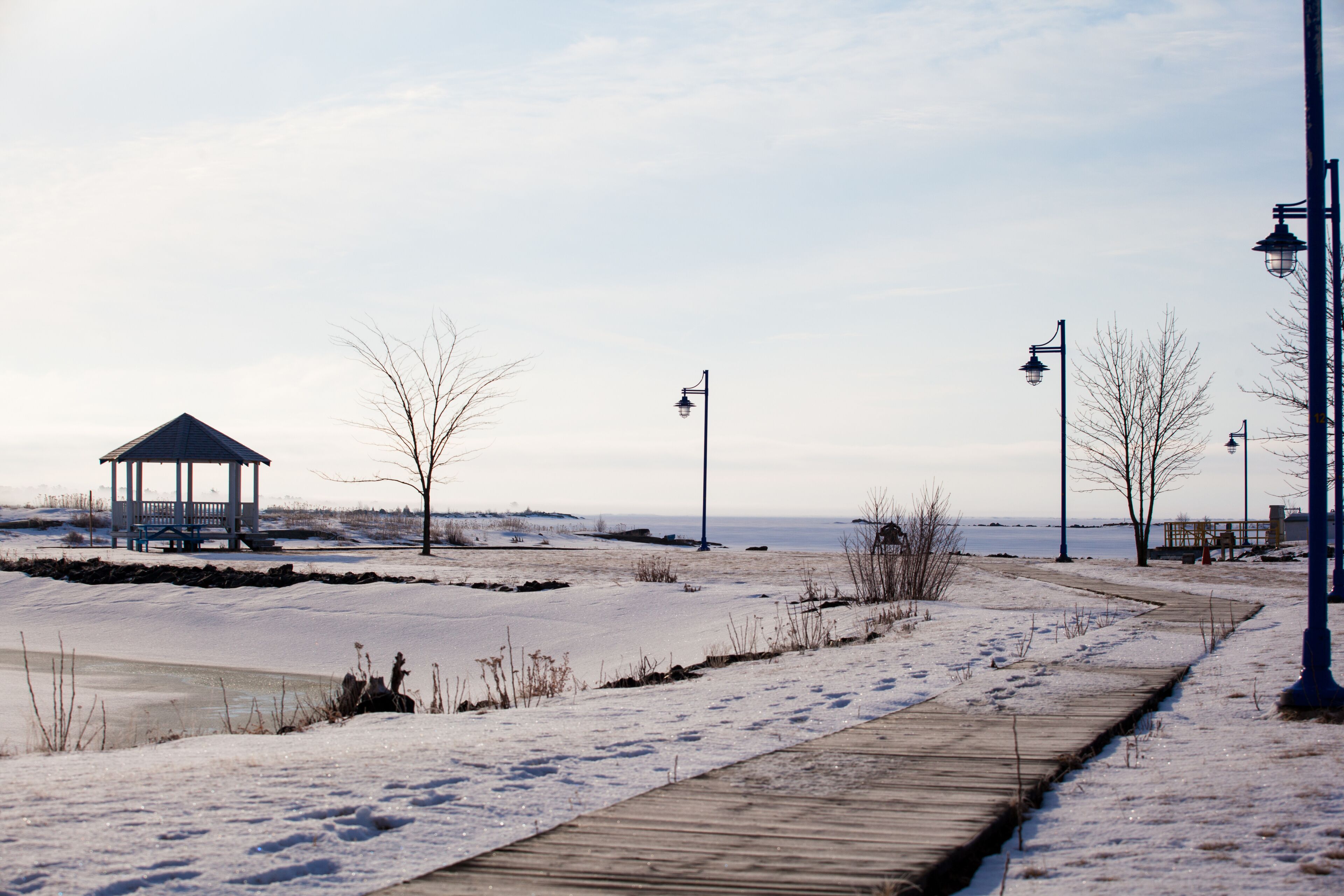 A snow-covered boardwalk, a gazebo, and a frozen body of water.