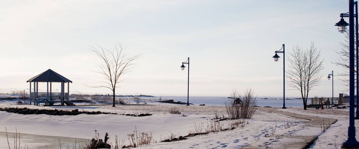 A snow-covered boardwalk, a gazebo, and a frozen body of water.